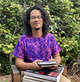 Author photo of Robert in bright purple shirt holding books in front of bushes