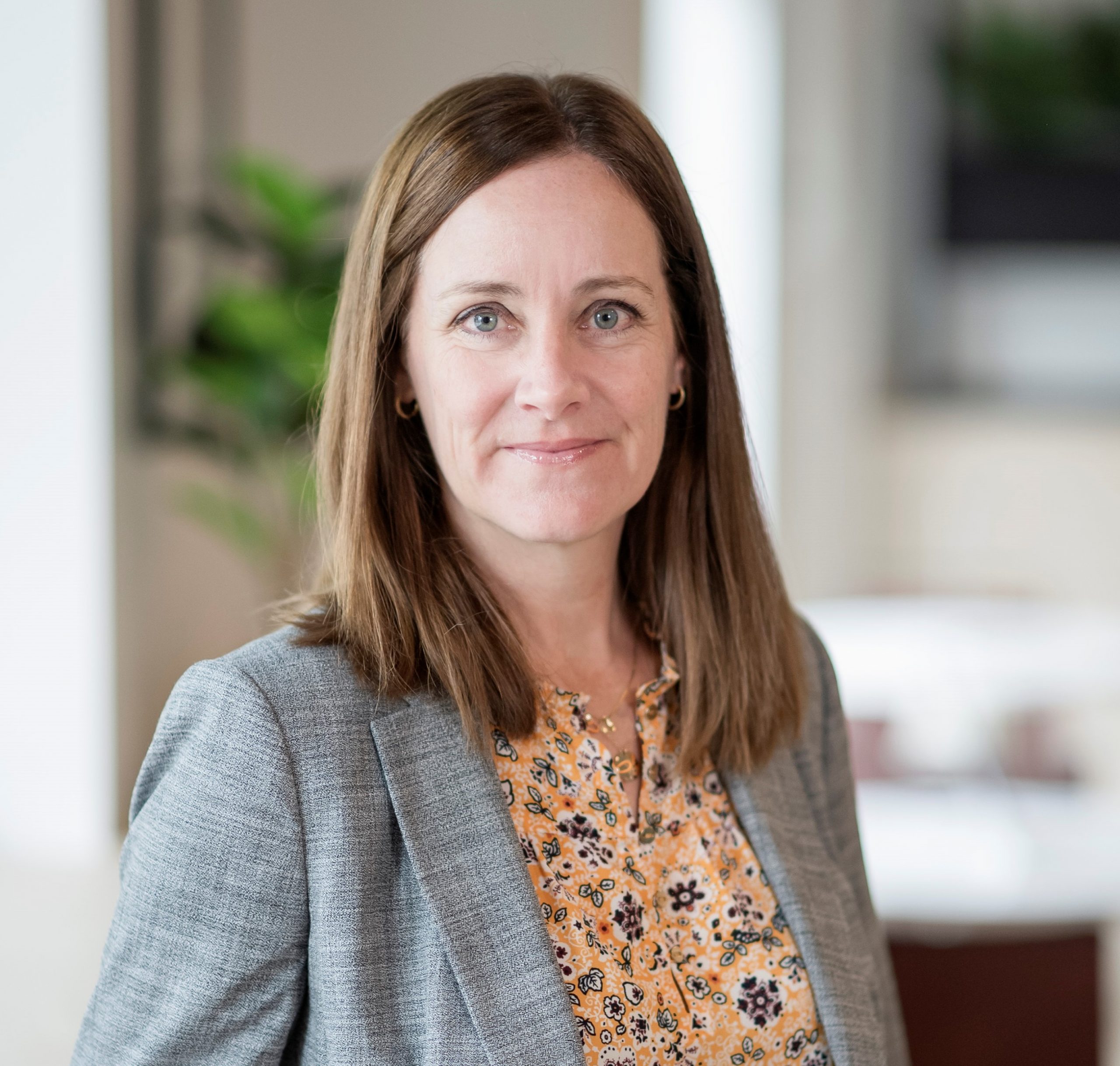 Shannon Keuter headshot: white woman with shoulder-length brown hair wearing a floral patterned shirt under a gray blazer