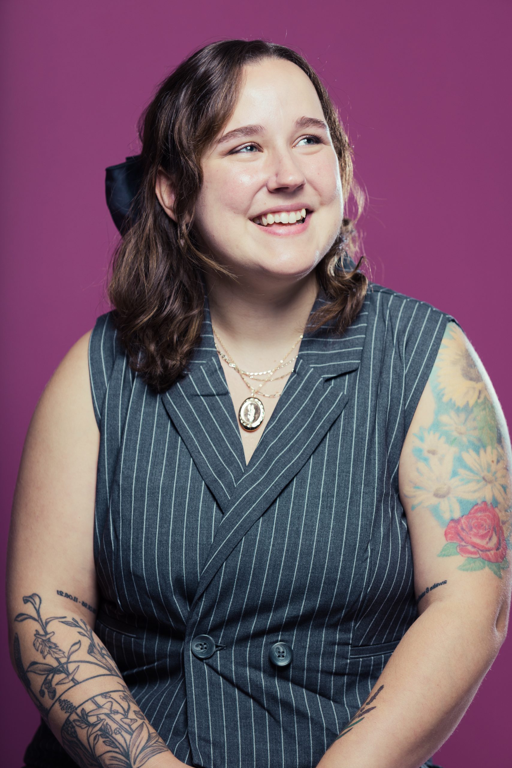 Kimm Topping headshot showing Kimm in a black and white pinstrikpe sleeveless suit with a purple background